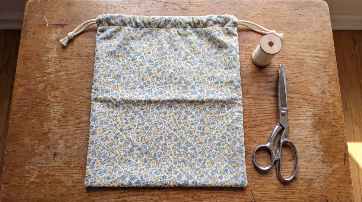 Simple finished drawstring bag in printed quilting cotton beside a spool of thread and fabric scissors