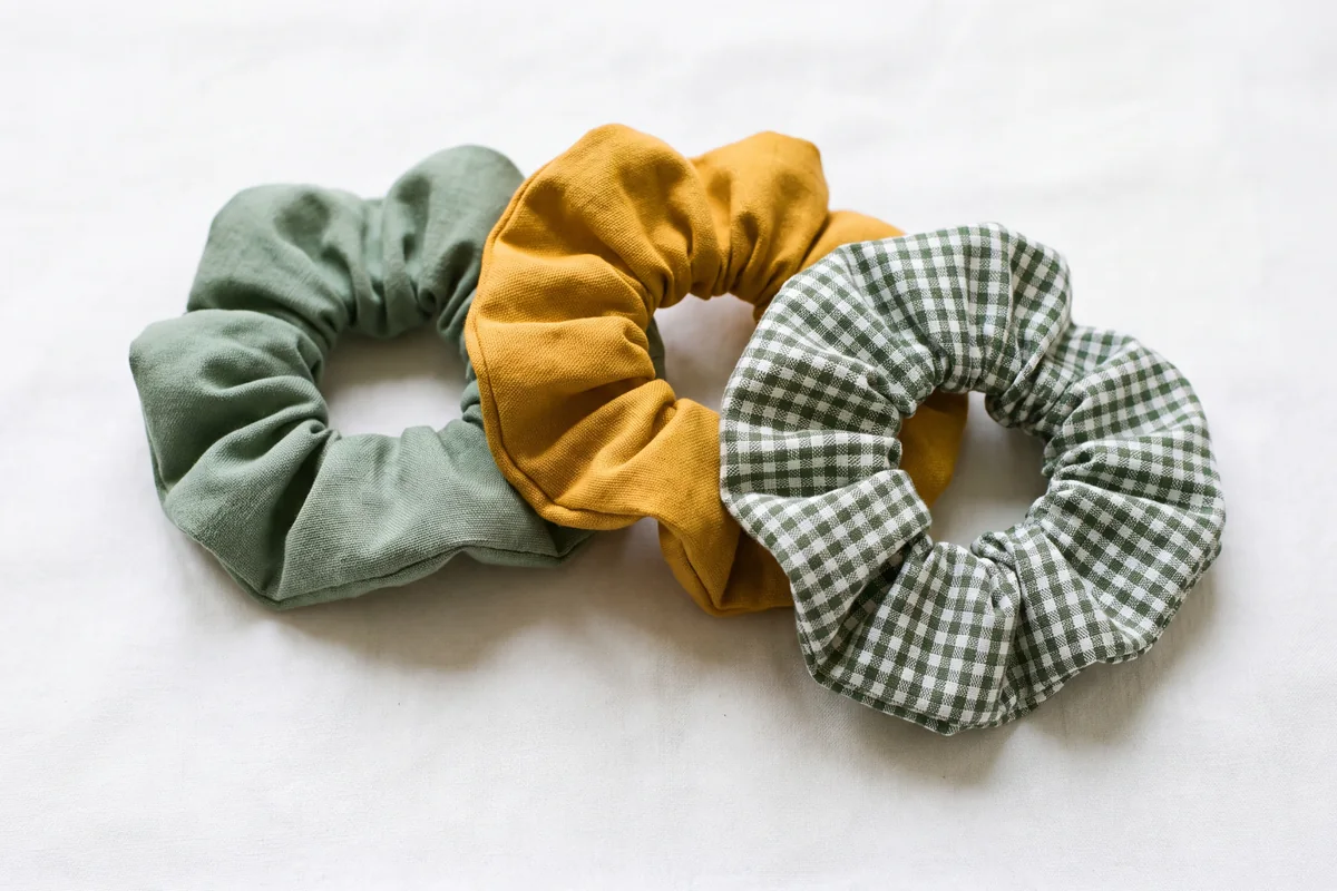Three cotton scrunchies in green, mustard and gingham check on a white surface